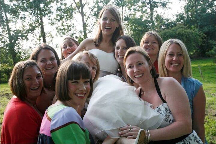 A bride hugged by a group of smiling friends on the lawn