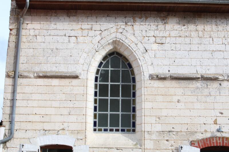 The white limestone wall of the old chapel with a tall pointed gothic window