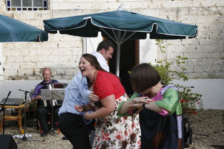 Two women laughing together in the courtyard under a parasol while a musician plays