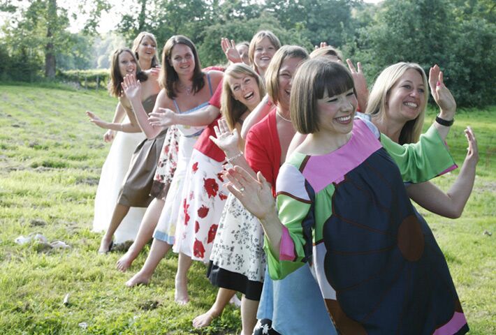A line of women in summer dresses dancing barefoot in the field