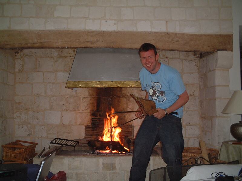 A man building up a log fire in a tall stone fireplace