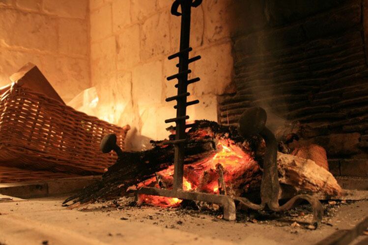 Logs burning in the big stone fireplace, with a wrought-iron fire dog and a log basket