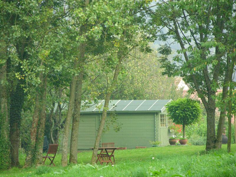 A green painted shed under tall trees, with two folding chairs on the lawn