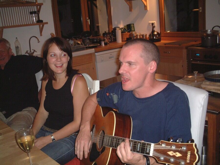 A guest playing guitar and singing at the kitchen table after dinner
