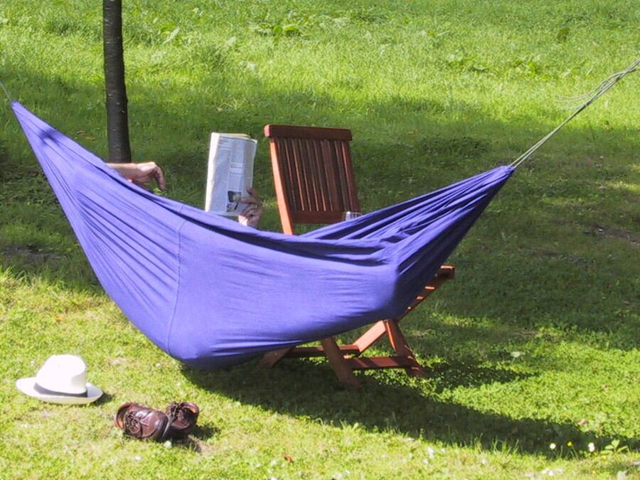 A purple hammock on the lawn in bright sunshine, a sun hat on the grass
