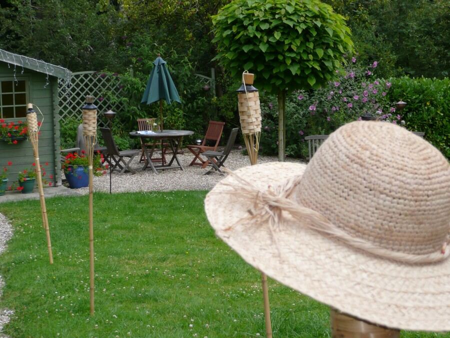 A straw sun hat on a garden torch in the foreground, the patio and parasol behind