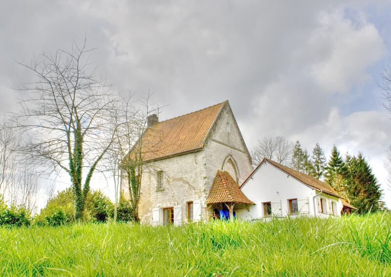 The white stone chapel and its wing seen across long spring grass under a pale sky