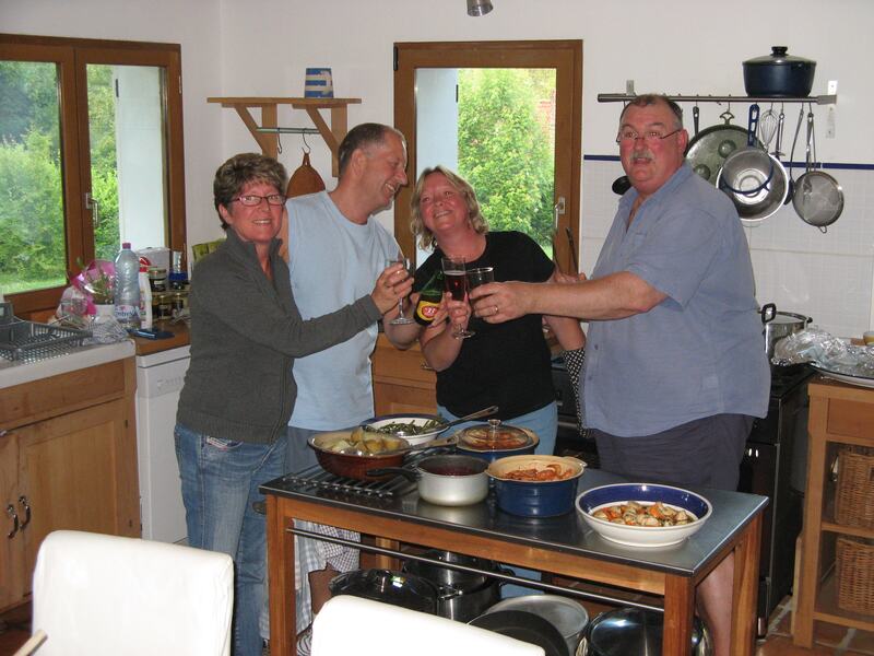 Four guests raising glasses round a cooker of steaming pans in the kitchen