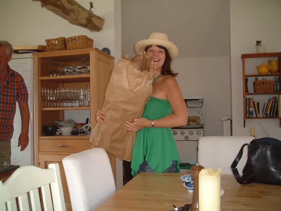 A guest in a sun hat holding a bag of shopping in the kitchen, beside the dresser and dining table