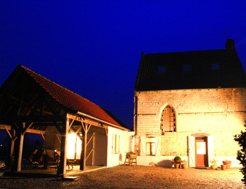 The house at dusk under a deep blue sky, lights glowing under the covered terrace and on the stone walls