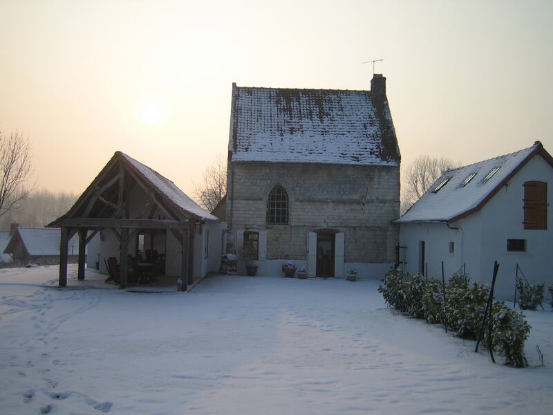 The house and courtyard under snow, a pale winter sun behind the trees