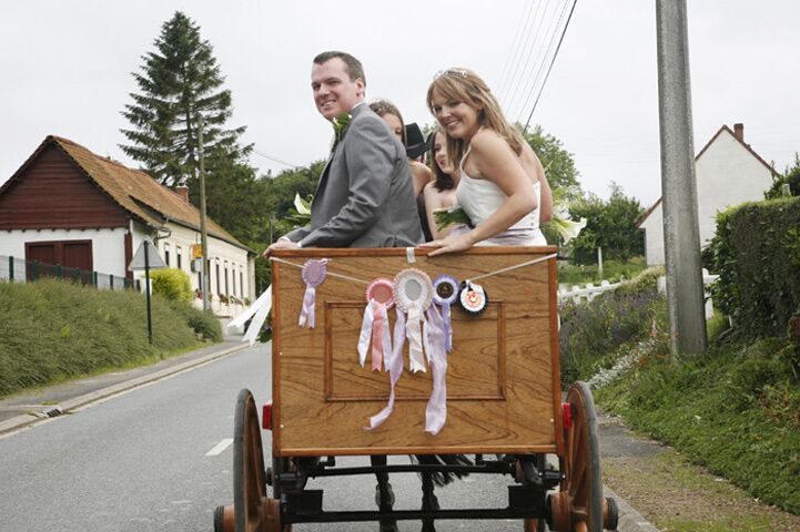 A bride and groom riding in a cart decorated with ribbons along a village lane