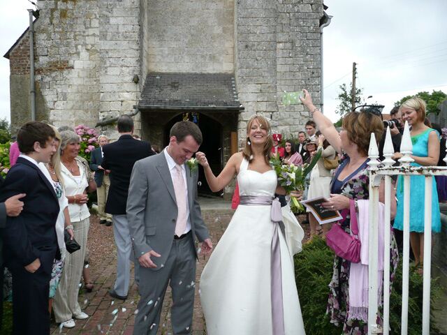 A bride and groom walking out of the village church as guests throw confetti